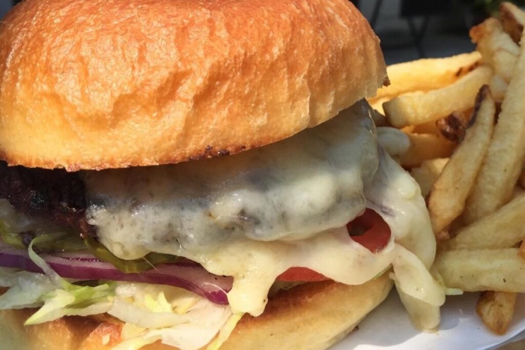 A closeup of a burger with cheese, tomato and lettuce and a side of fries.