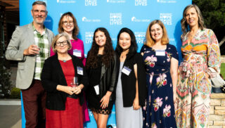 A smiling group of attendees poses in front of the Ritter Center step-and-repeat banner, celebrating community partnerships and support.