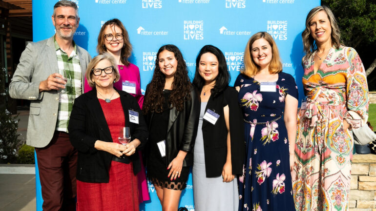 A smiling group of attendees poses in front of the Ritter Center step-and-repeat banner, celebrating community partnerships and support.