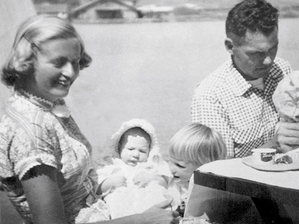 Black and white photo of a smiling family with a baby and small child sitting outdoors by a lagoon.
