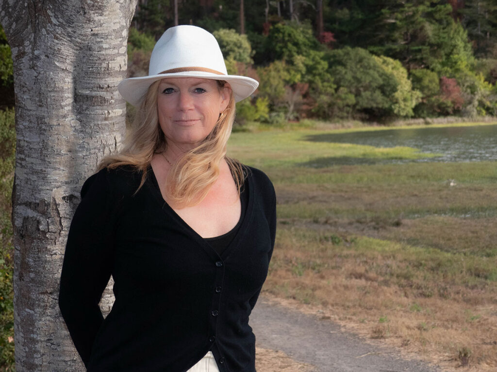 A woman wearing a hat and a black sweater poses, exuding a relaxed and fashionable vibe standing next to a tree.