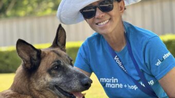 A woman in a blue shirt and large brimmed white hat stands with a dog.