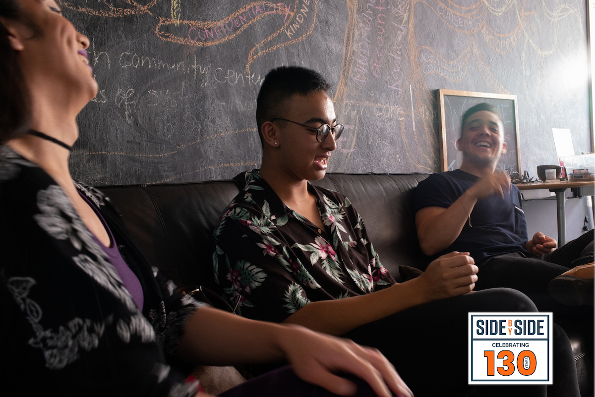 Three people sitting on a couch in front of a chalkboard wall.