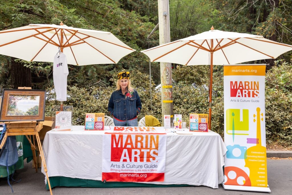 2024 MV Fall Arts Festival Marin Arts sponsor booth, with umbrellas, a poster, and things on the table.