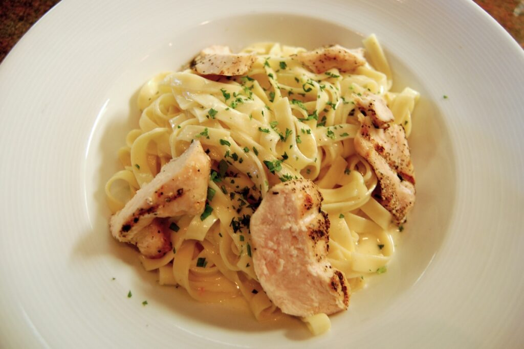 A bowl of pasta topped with herbs and slices of white meat.