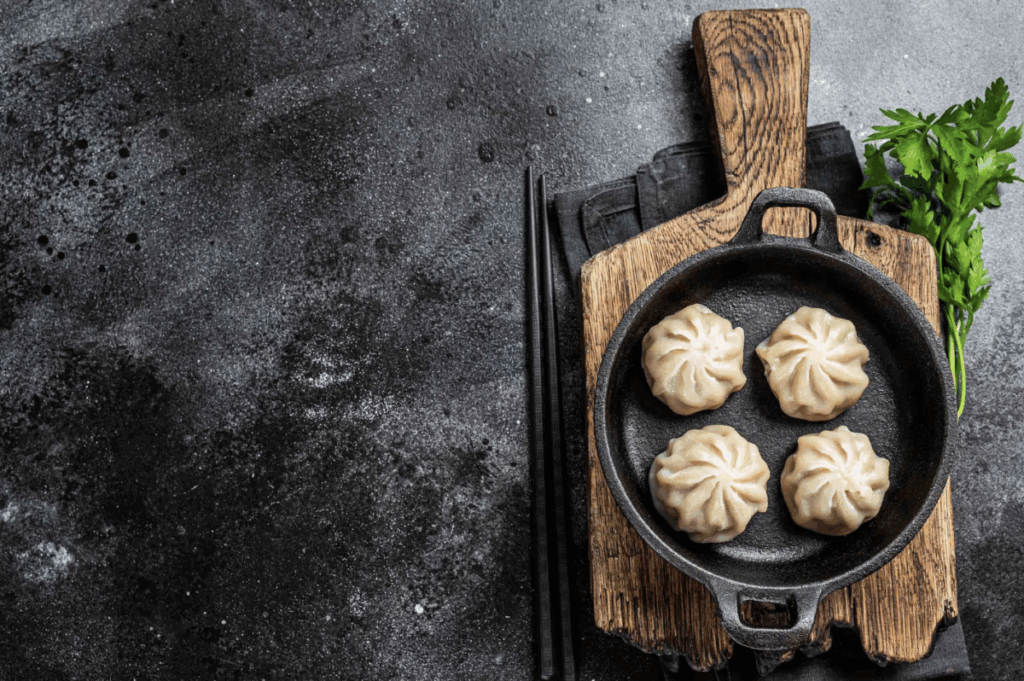 A cast iron pan with dumplings on top of a wooden cutting board.