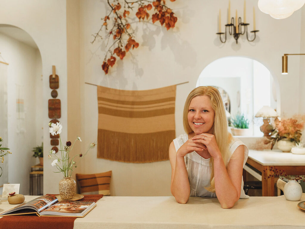 A woman seated at a table in a warm, inviting home environment, appearing contemplative.