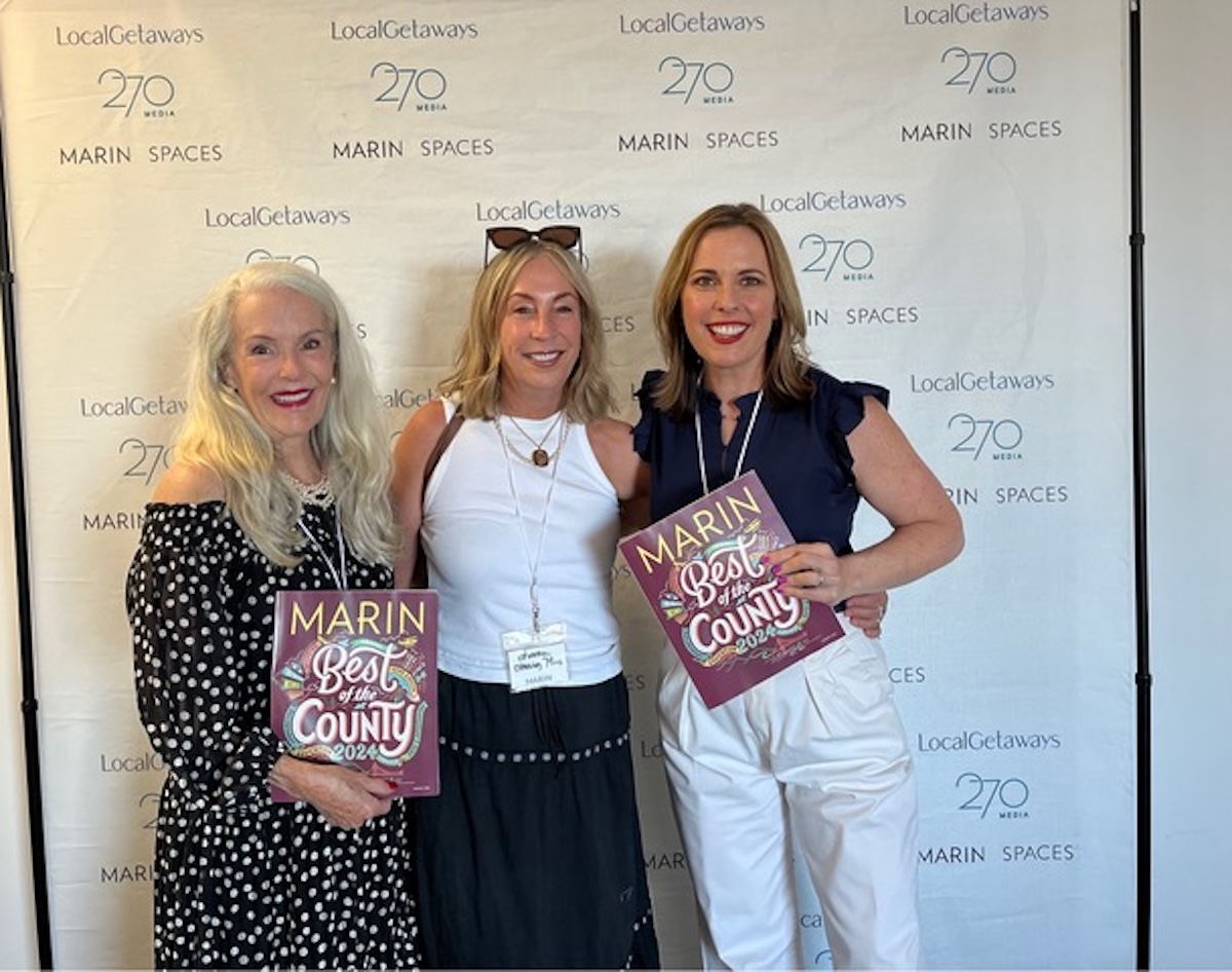 Three women holding magazines stand for a picture.