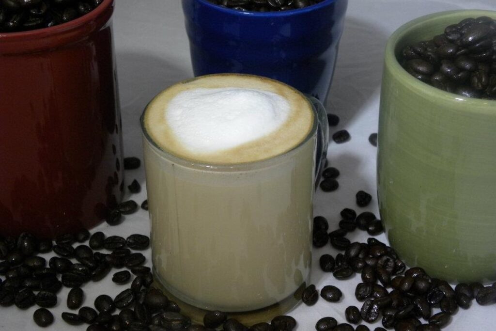 A latte sitting on a table surrounded by three cups of coffee beans.