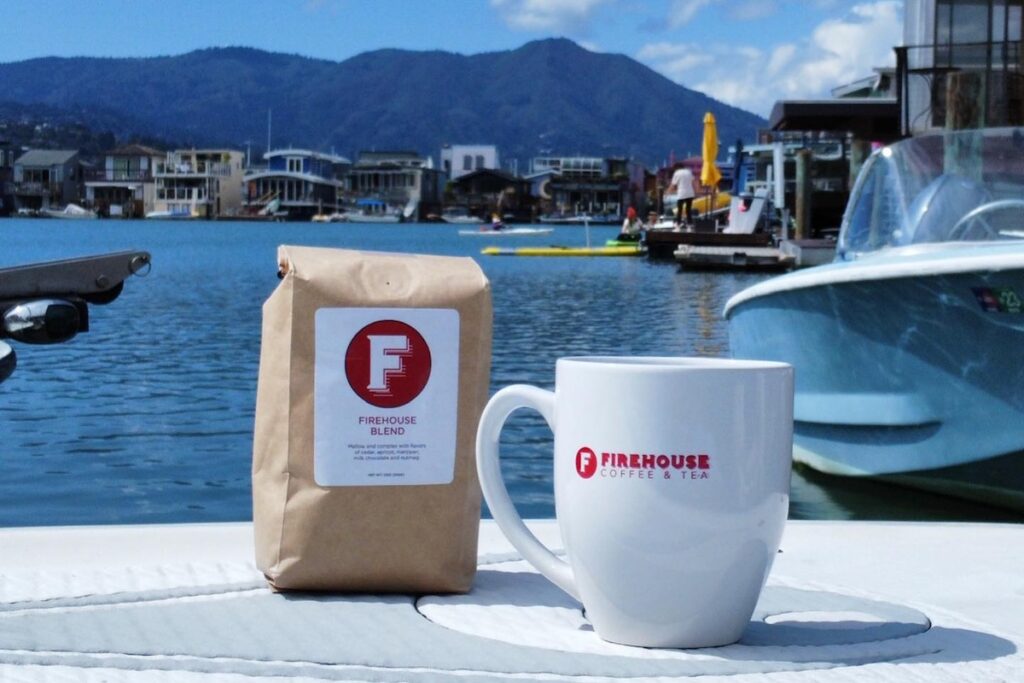 A coffee mug and bag of beans sits against a backdrop of a boat harbor.