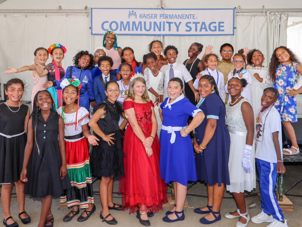 Performing Stars children smiling brightly on the Kaiser Permanente Community Stage in colorful, formal, and cultural attire.