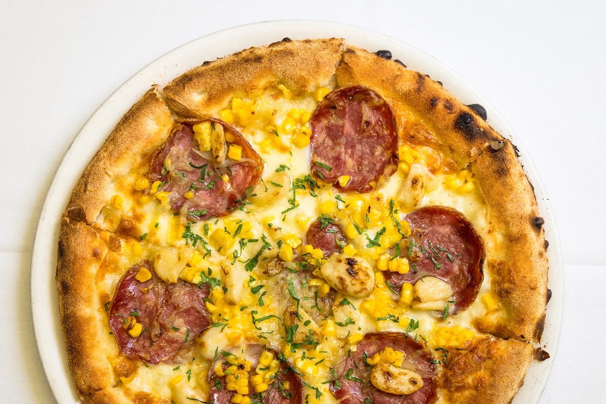 An aerial shot of a pizza with pepperoni, corn and other toppings.