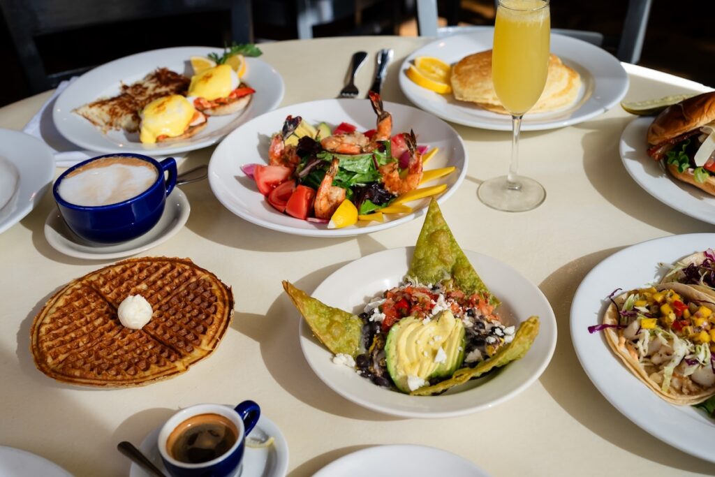 A table with various brunch foods including waffles, eggs benedict and more.