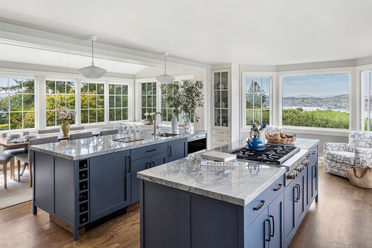 A kitchen with gray cabinetry, marble countertops and a view from the windows all around.