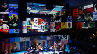 Musicians perform on stage with colorful jazz album artwork projected across the walls.