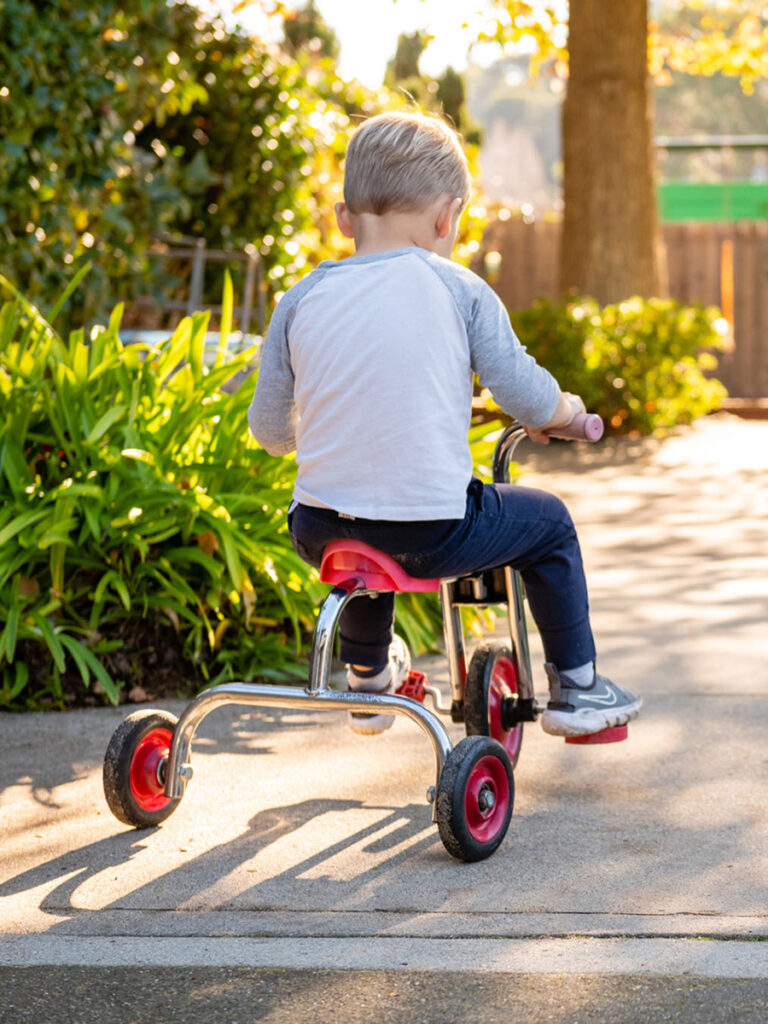 A young boy rides a tricycle along a sidewalk, enjoying a sunny day outdoors.