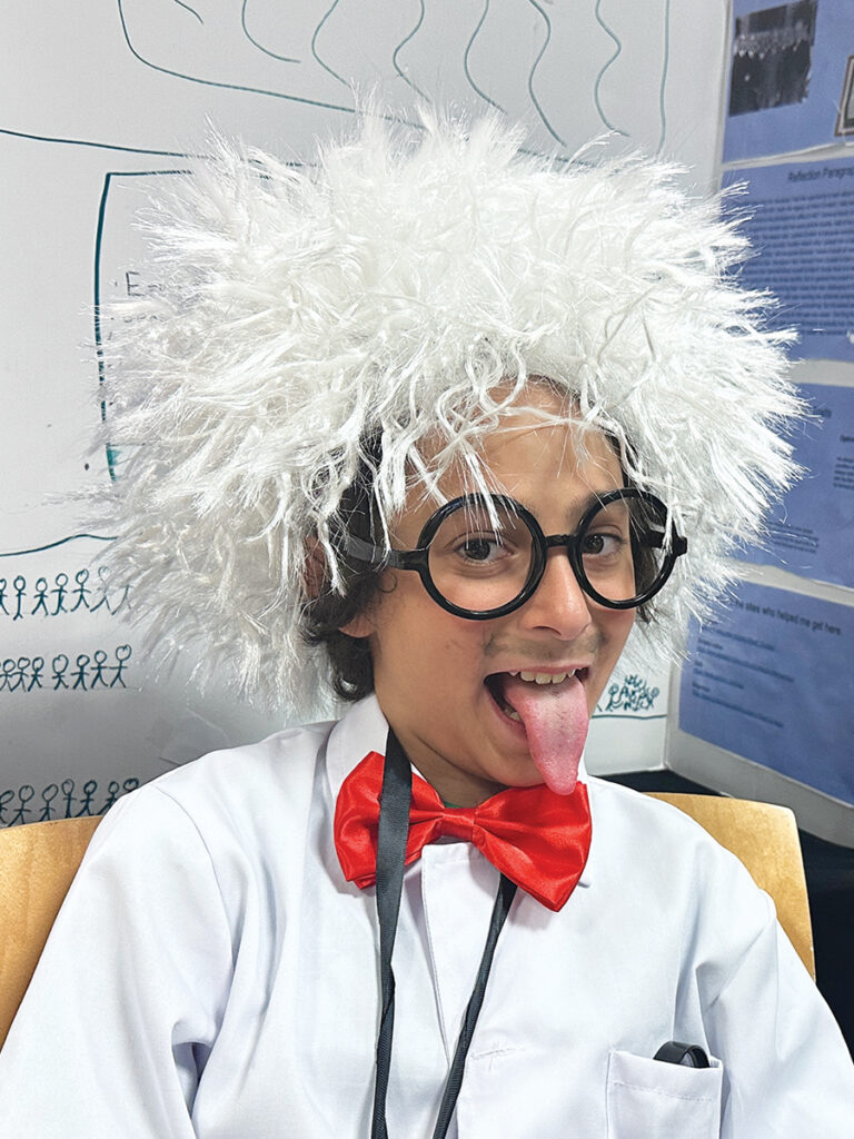 A boy wearing a white wig and a red bow tie, smiling and posing for the camera.