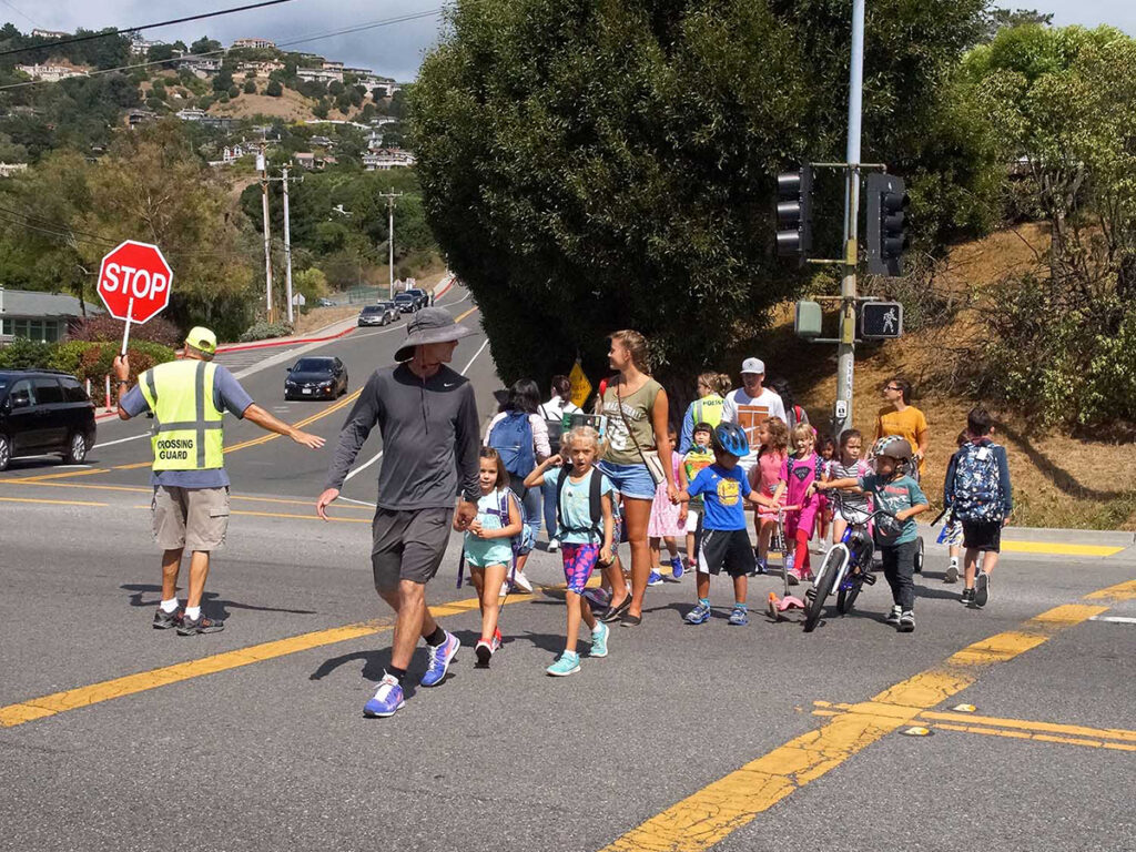A crossing guard holds a stop sign while guiding a group of children and adults safely across a street.