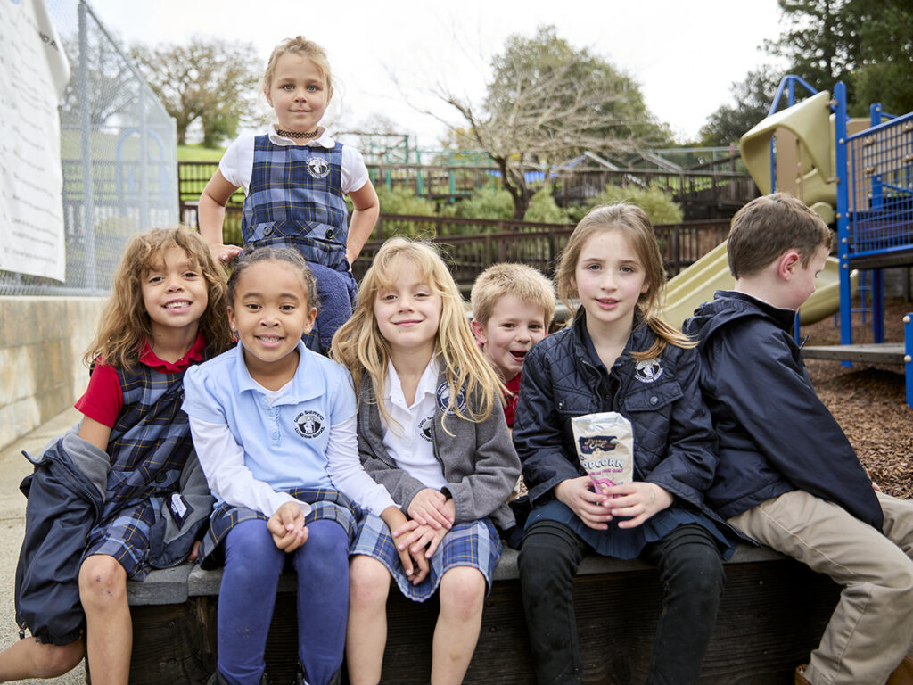Several children seated on a bench, enjoying each other's company in a sunny outdoor setting.