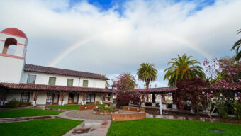 A colorful rainbow stretches over a peaceful courtyard, enhancing the beauty of the sky and surrounding area.