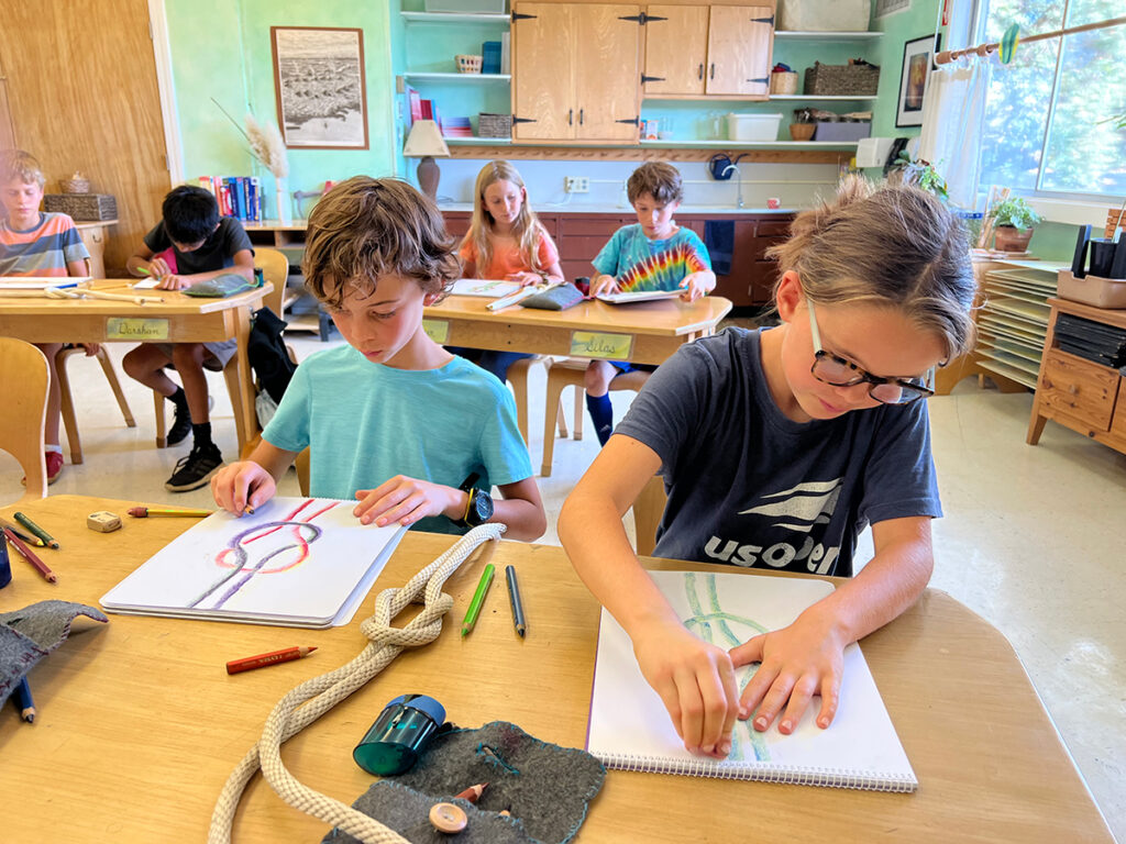 A group of children engaged in various art projects at desks in a bright classroom, showcasing creativity and collaboration.