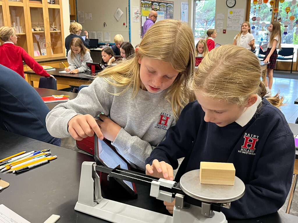 Two girls work together on a science project in a lab, focused on their tasks with various scientific tools around them.