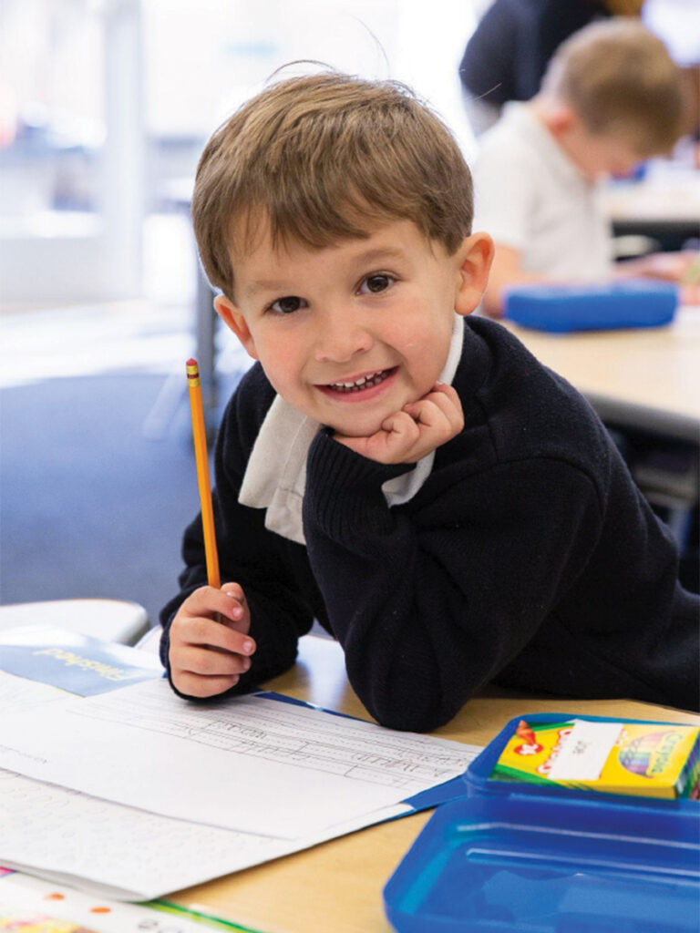 A young boy sits at a desk, focused on writing with a pencil in hand.