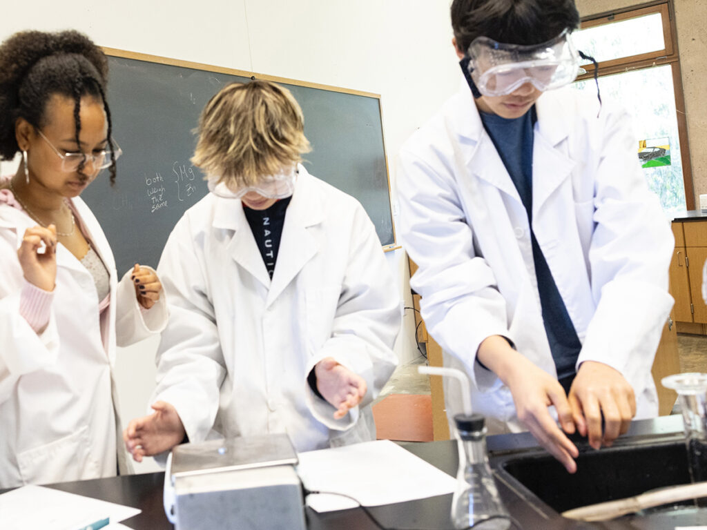  A team of students wearing white lab coats focused on conducting experiments in a laboratory environment.
