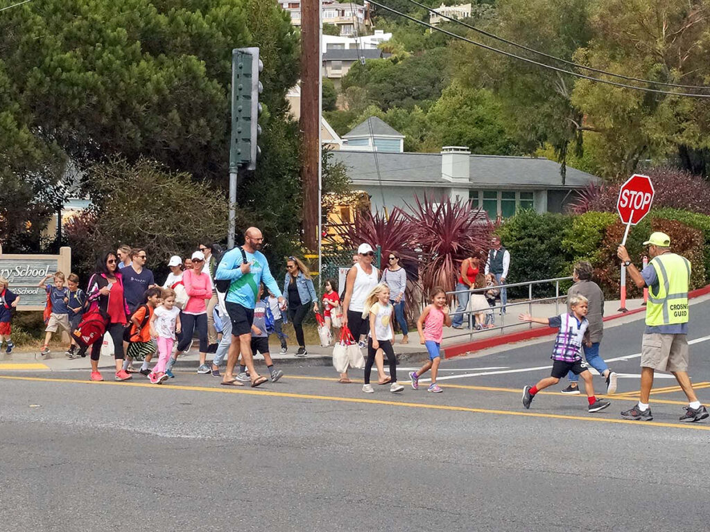 A crossing guard holds a stop sign while guiding a group of children and adults safely across a street.