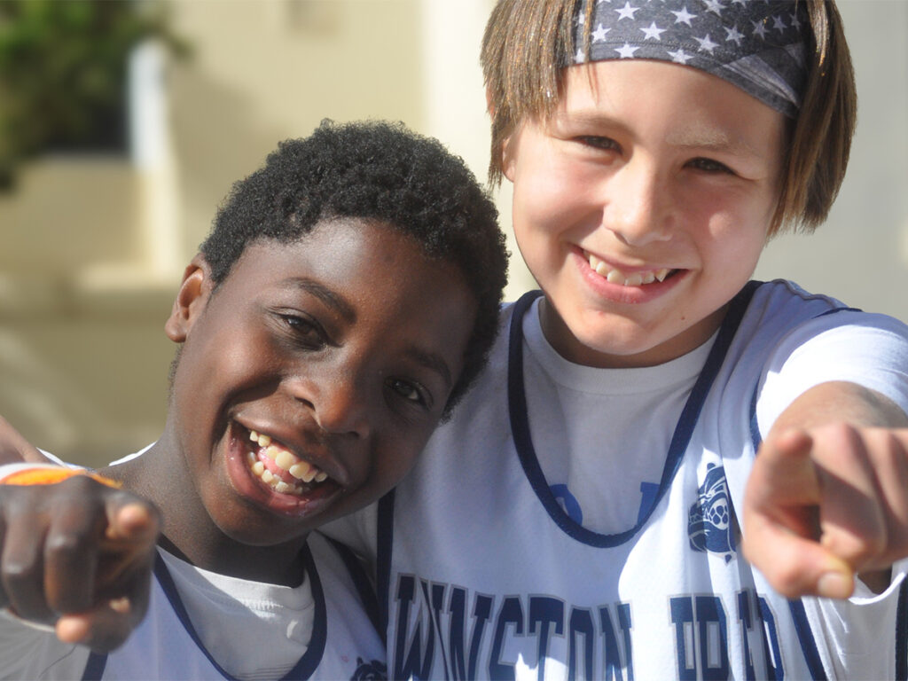 Two boys dressed in white shirts, looking cheerful while standing in a casual pose.
