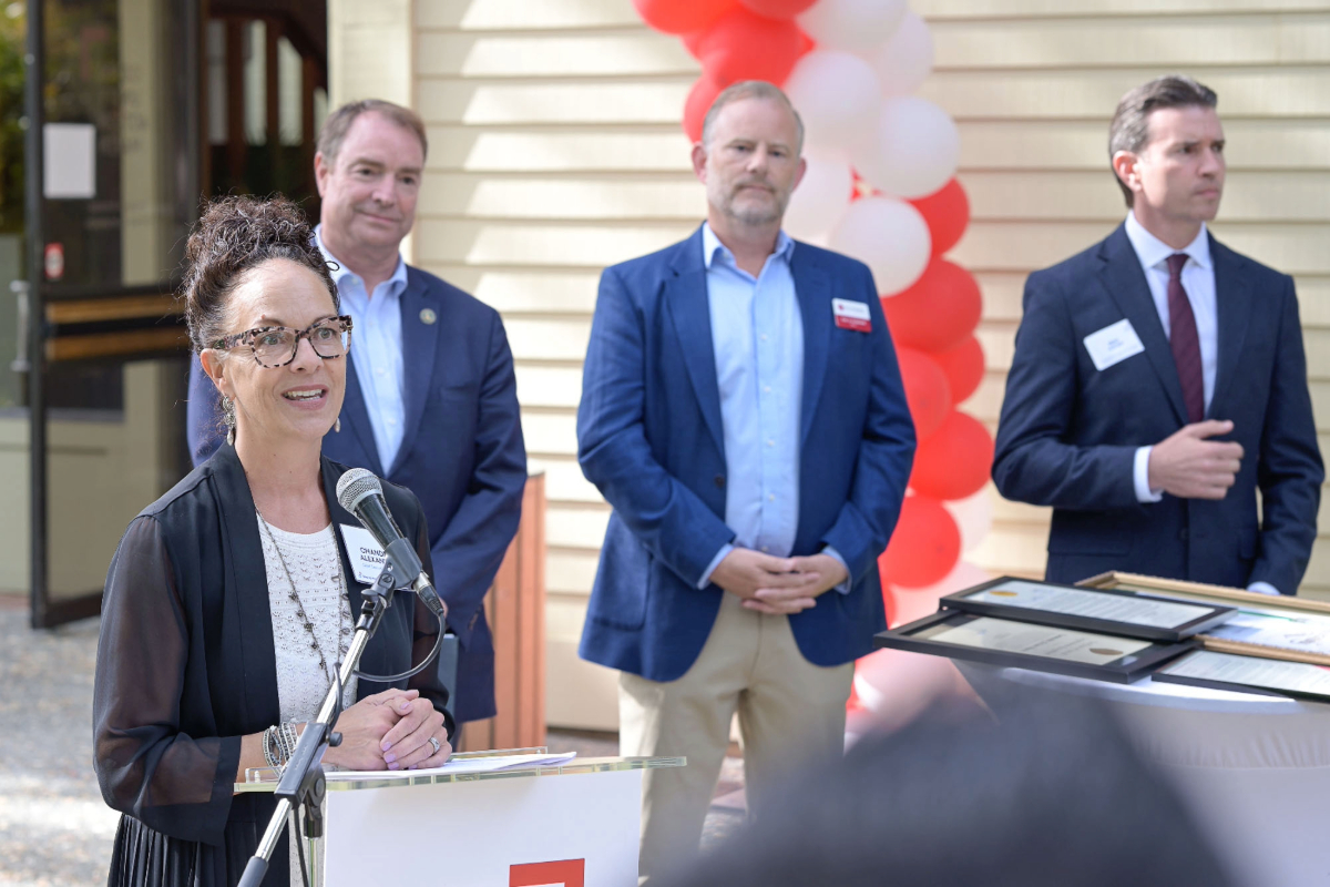 A large crowd gathers outside Community Action Marin’s new Novato campus, facing a stage framed by a red and white balloon arch during the Step Up Marin program.