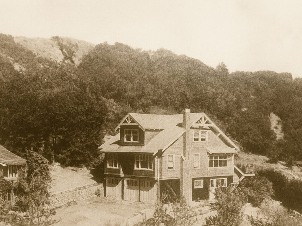 Historic sepia-toned photograph of the original 1925-era Mill Valley craftsman home, nestled among trees at the base of the hillside.