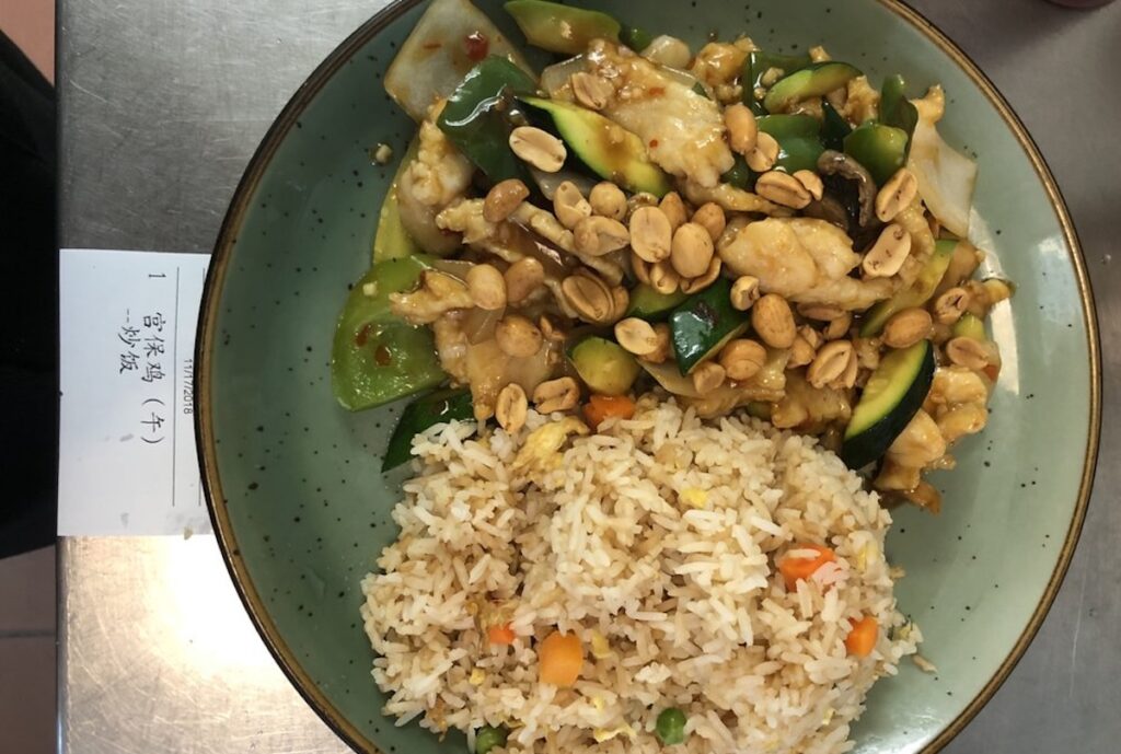 A bowl with some fried rice and veggies with peanuts.