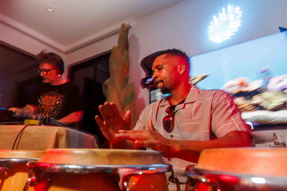 A musician plays conga drums while a DJ mixes tracks in the background under colorful lighting at the fundraiser.