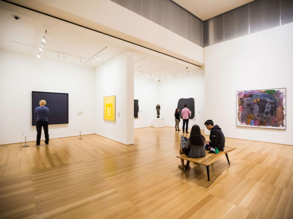 Gallery with people viewing modern art paintings and sculptures.