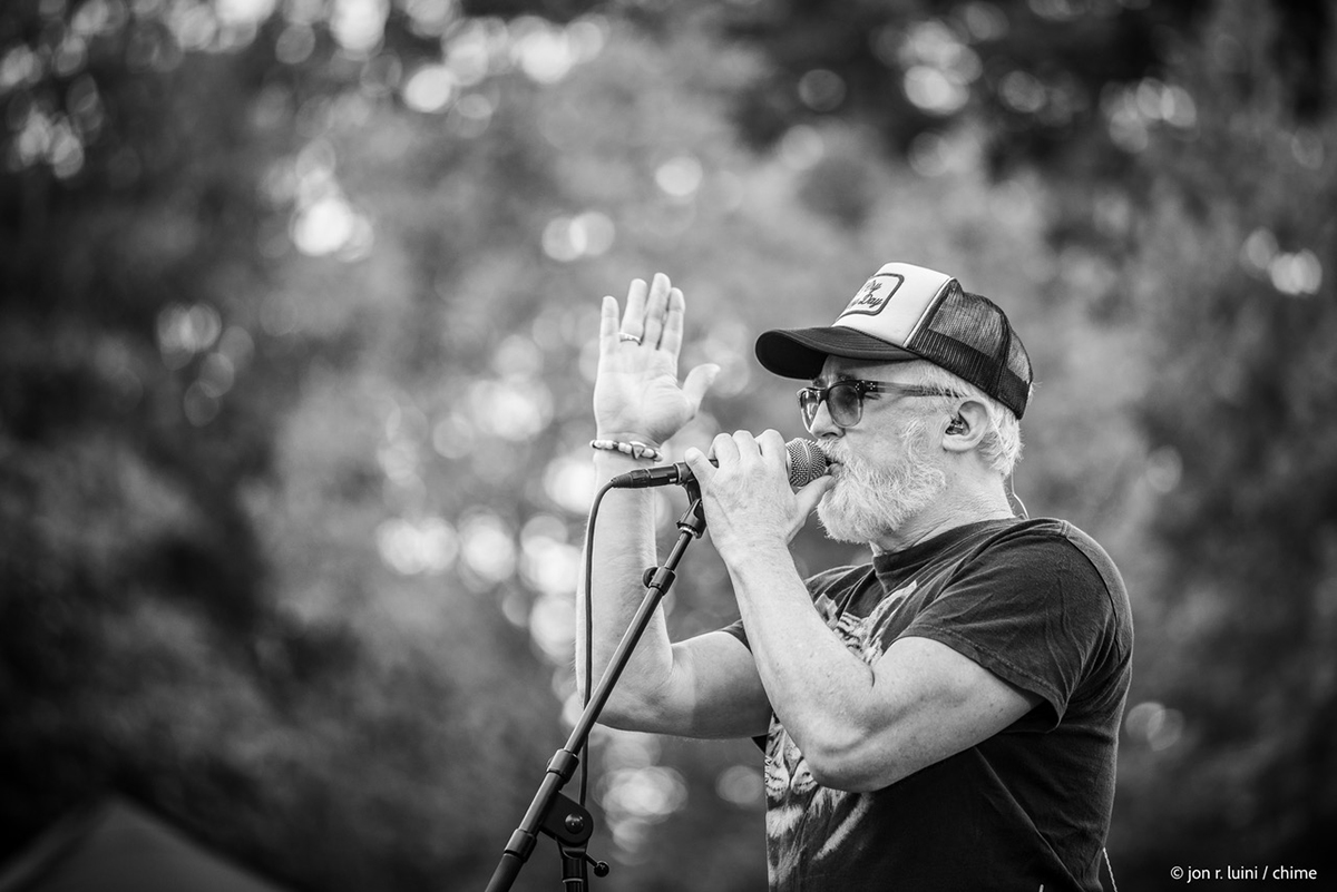 John McCrea, the bearded lead singer of CAKE, captivates the audience while singing into a microphone.