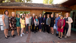 A group of women smiling standing together in front of a building.