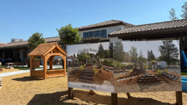 A playground featuring a prominent sign that reads "The Big Hill," surrounded by play equipment and green grass.