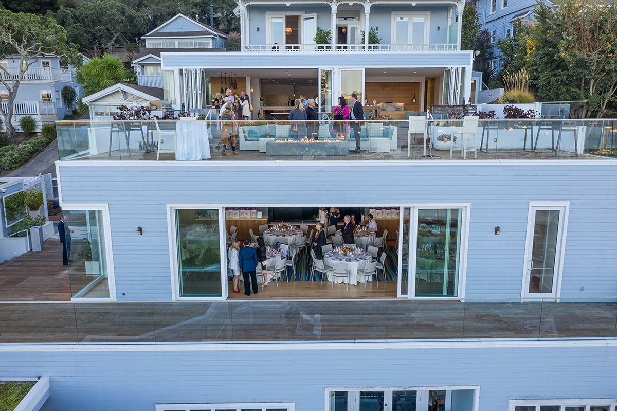 Aerial perspective of a wedding on a house rooftop, highlighting guests, decor, and the surrounding city skyline.