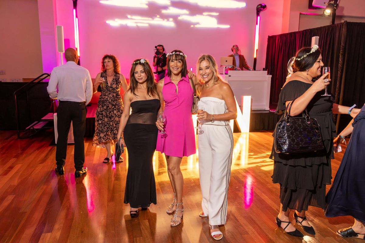 Three women posing stylishly near the DJ booth and glowing MARIN sign.
