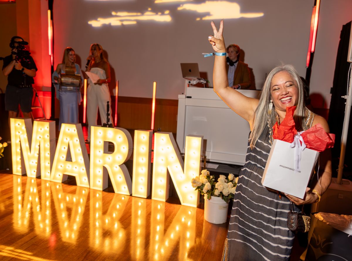 Woman smiling and holding raffle gift bag, flashing peace sign.