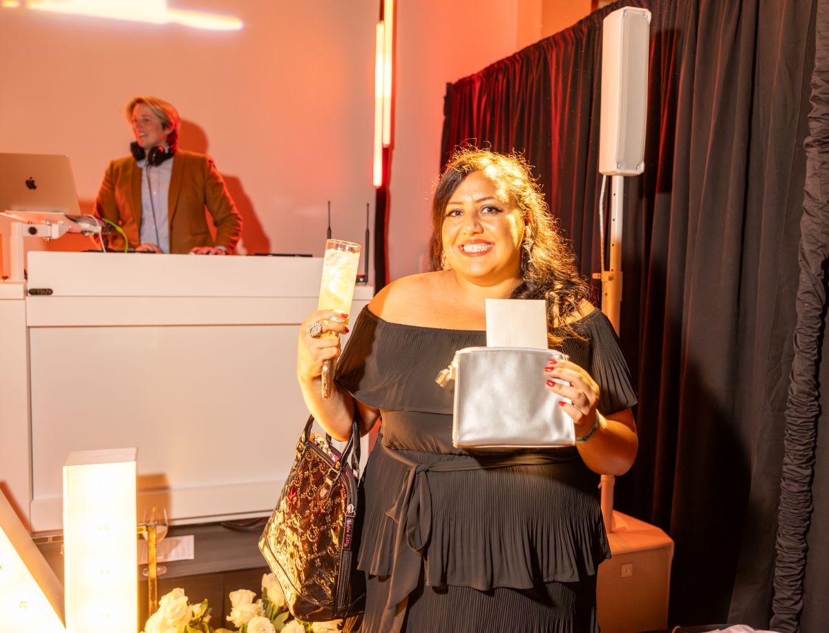 Woman smiling and holding raffle prizes with a drink.