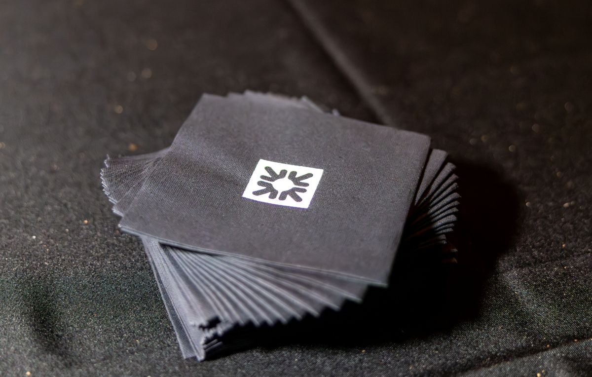 Stack of black cocktail napkins with white logo.