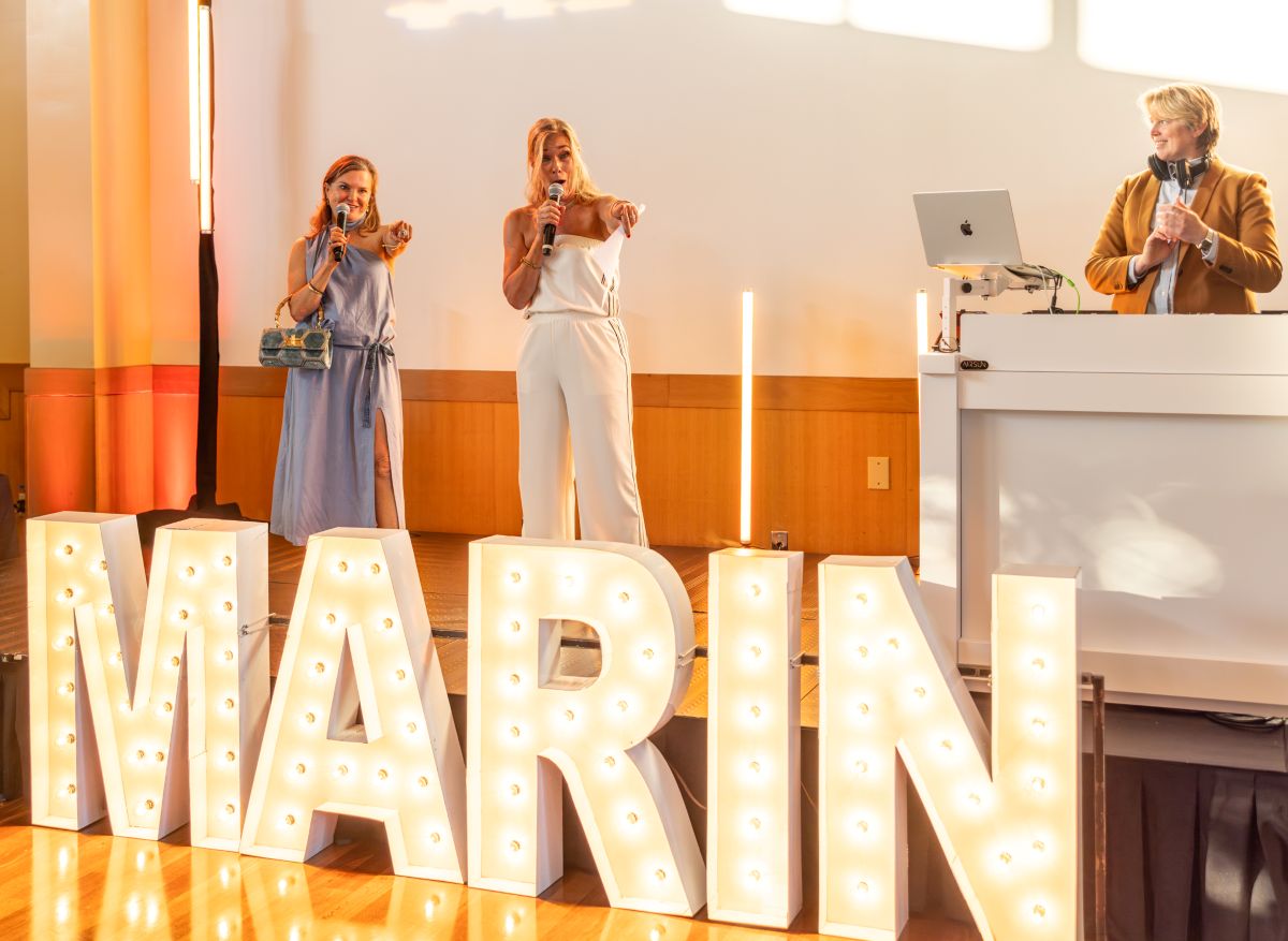 Hosts on stage with DJ behind large MARIN sign.