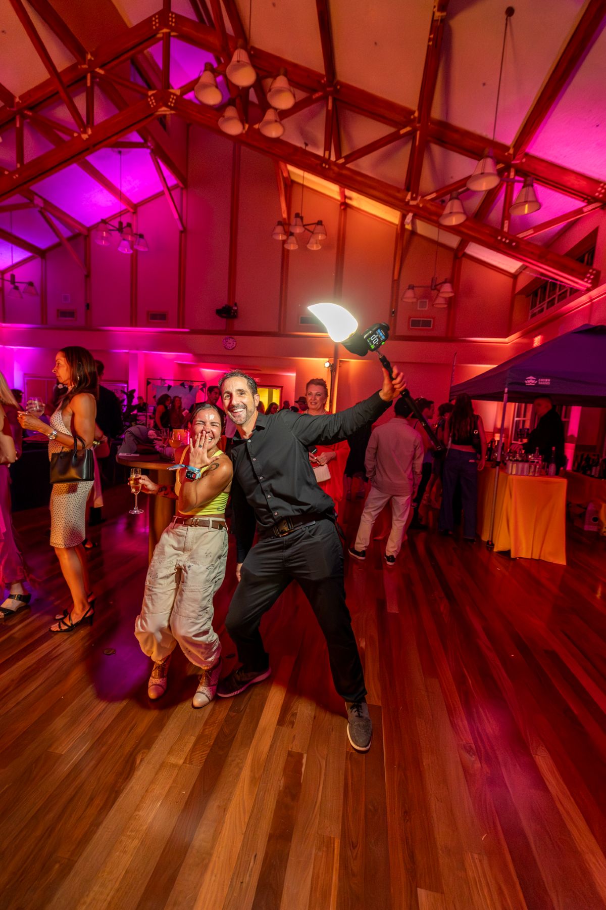 Guests laughing and posing with selfie stick on dance floor.