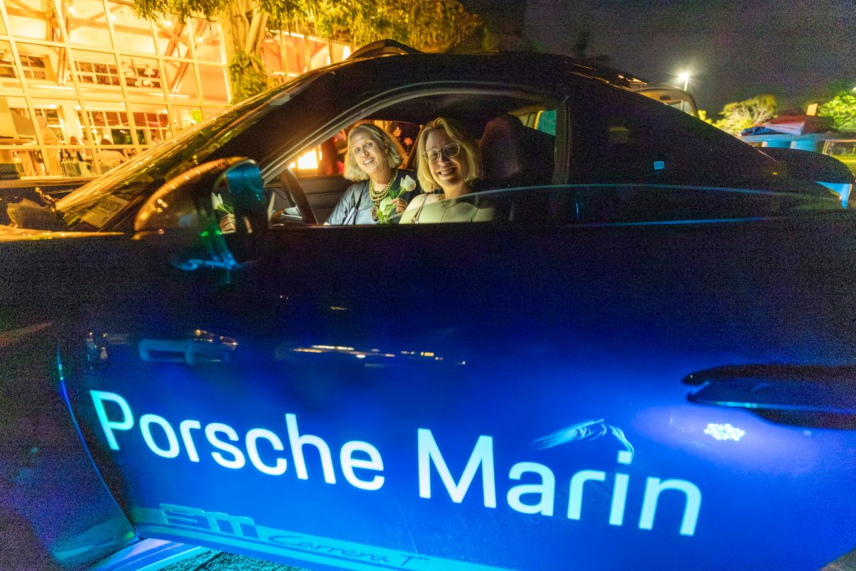 Two women smiling inside Porsche Marin car at night.