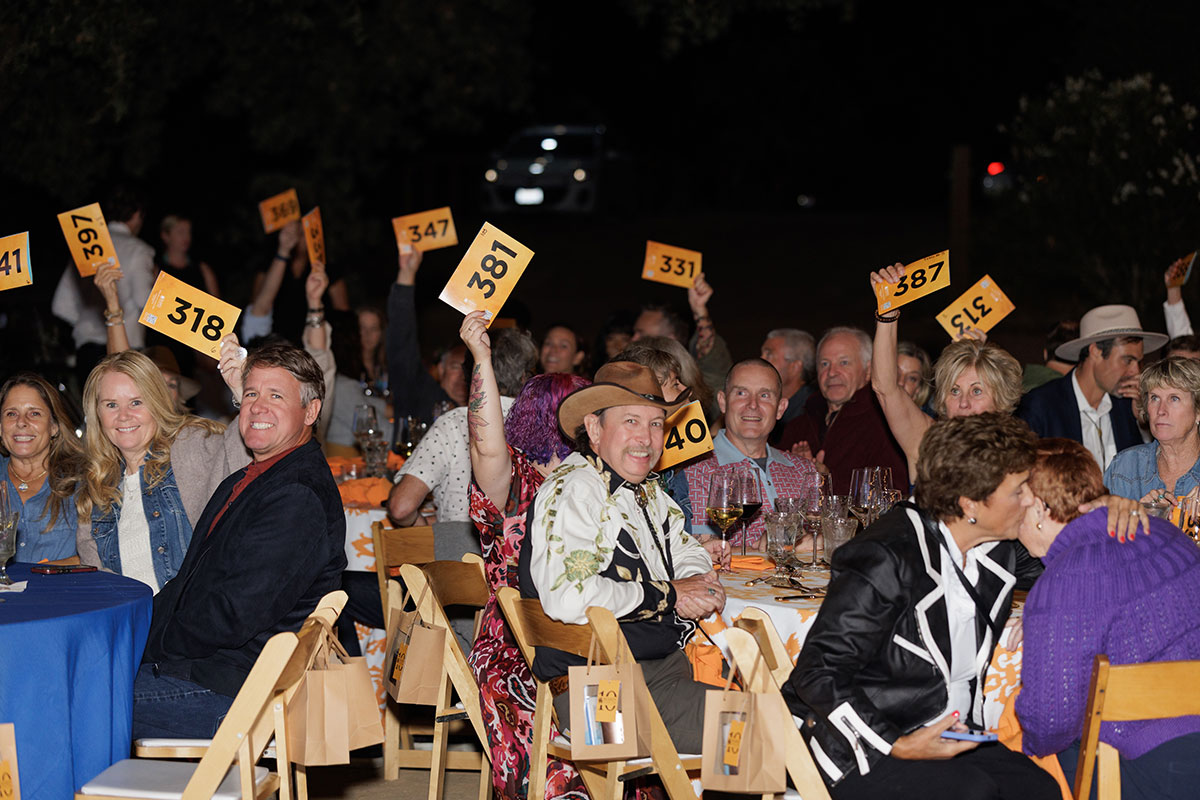 A group of people at tables, displaying auction numbers, showcasing their support for a cause