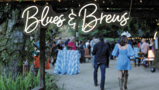 A colorful sign that says "Blues and Brews" at an outdoor festival, inviting guests to enjoy music and drinks.
