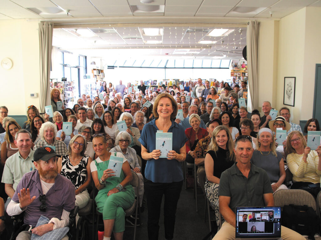 A large group of diverse people gathered in a public space, at a book launch, engaging in conversations and activities.