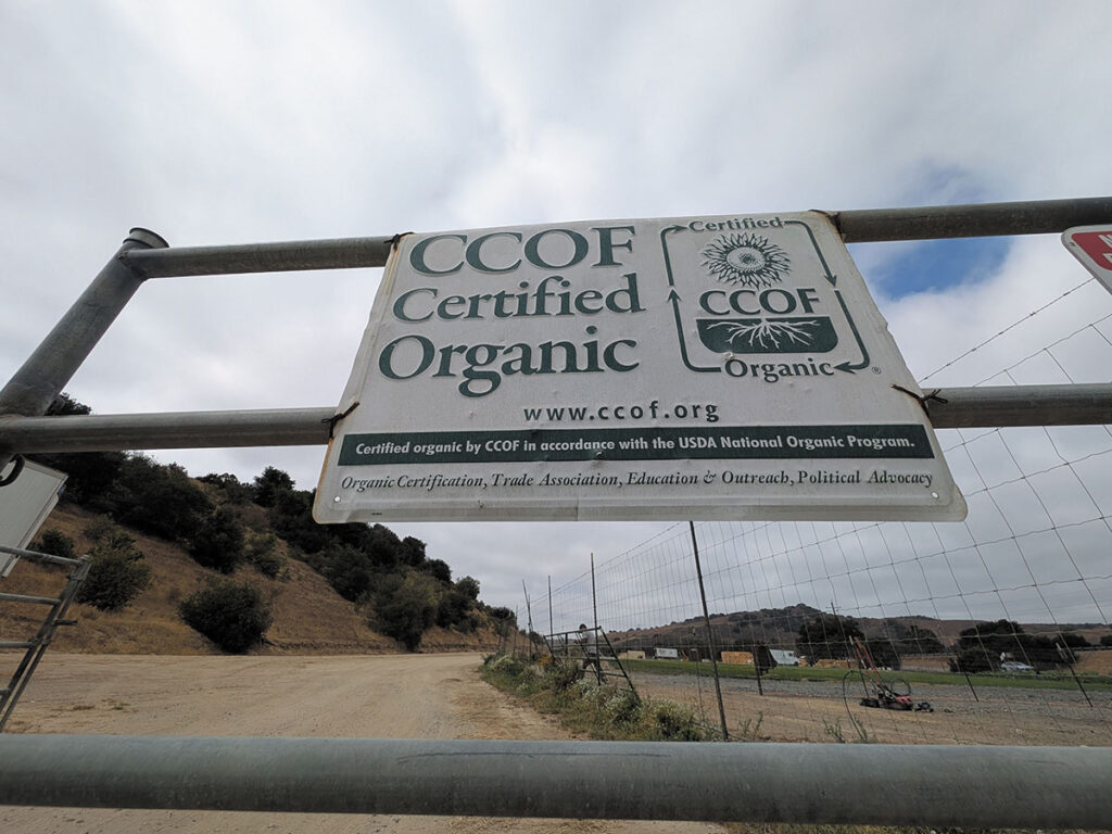  A sign reading "Certified Organic" attached to a wooden fence in a rural setting.